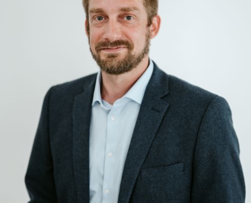 Cody Arendt headshot. Cody wears a dark blazer over a light-colored button-up shirt.