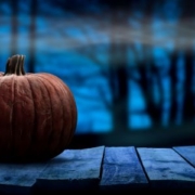 Large orange pumpkin on the left with a dark forest scene in the background. The background includes white fog over black, dark blue, and dark purple colors.