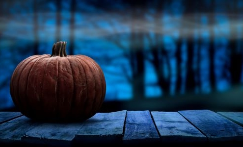 Large orange pumpkin on the left with a dark forest scene in the background. The background includes white fog over black, dark blue, and dark purple colors.